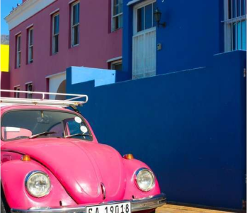 um fusca rosa na frente de uma casa azul do lado de outro predio rosa