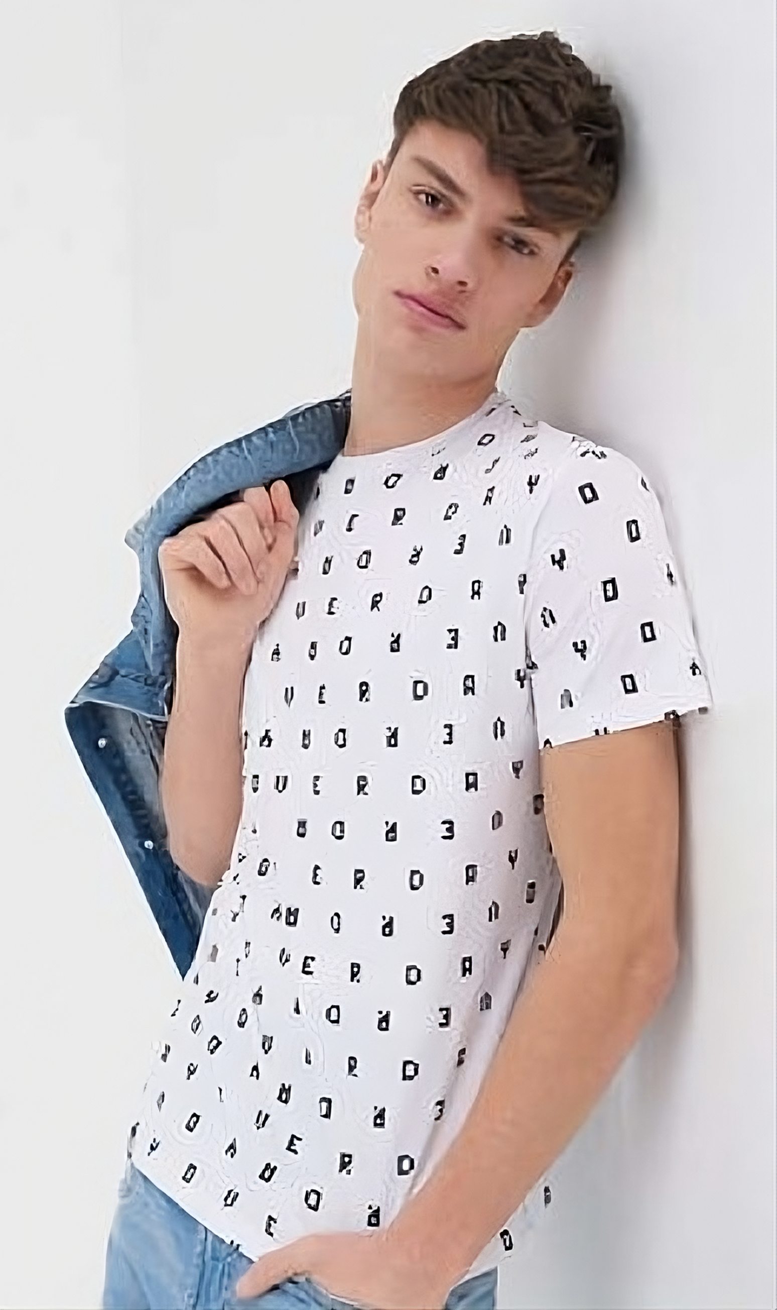 um rapaz posando segurando uma jaqueta jeans, e uma blusa branca com estampa de letras